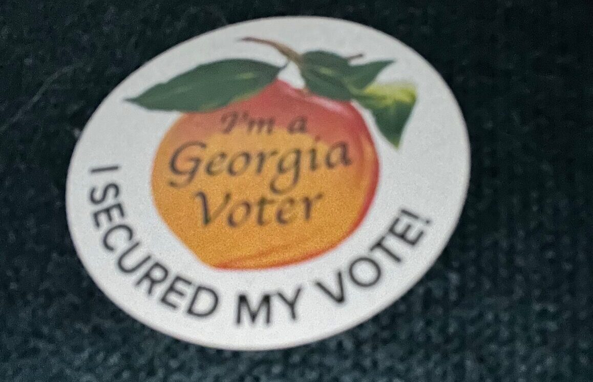 Close-up view of the "Georgia Voter: I Secured My Vote" sticker, with the phrase "Georgia Voter: I Secured My Vote" superimposed over the image of a peach.